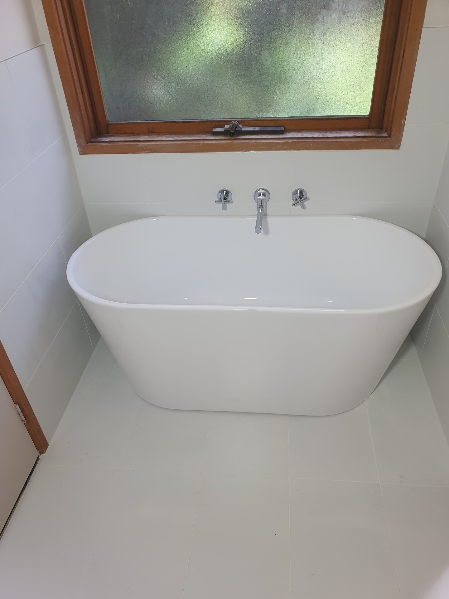 Freestanding bath with wall-mounted chrome tapware beneath frosted window