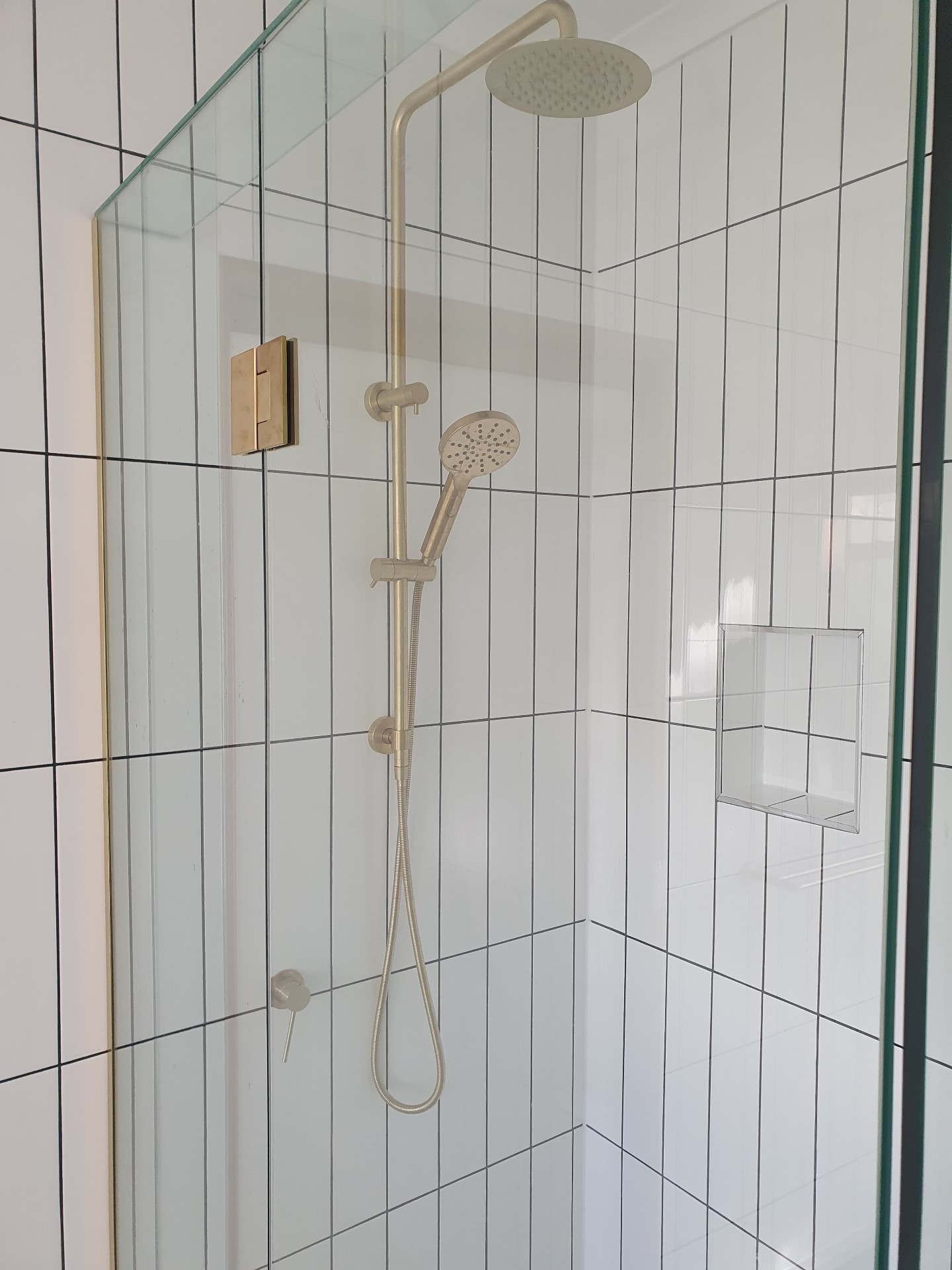 Detail of brushed brass shower fittings and tiled niche
