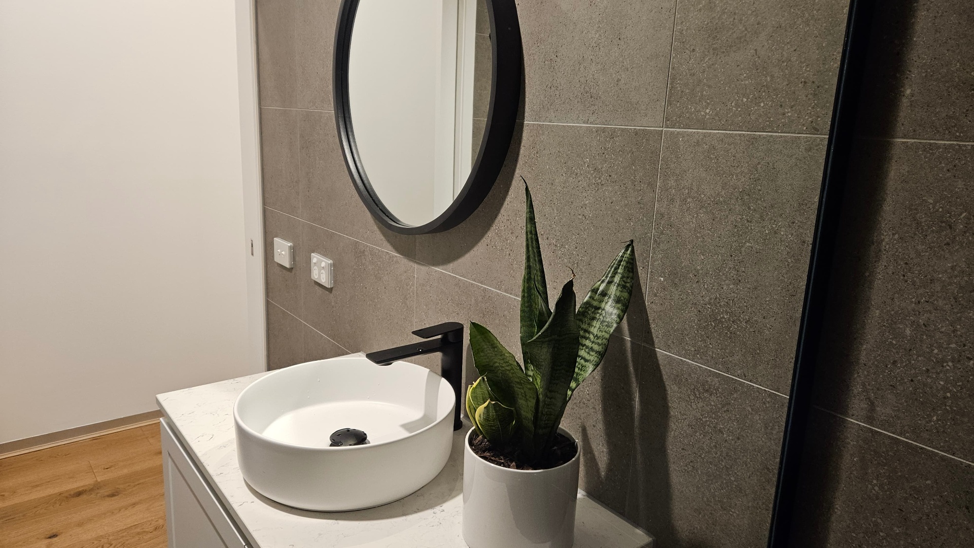 Round black-framed mirror above stone vanity with vessel basin