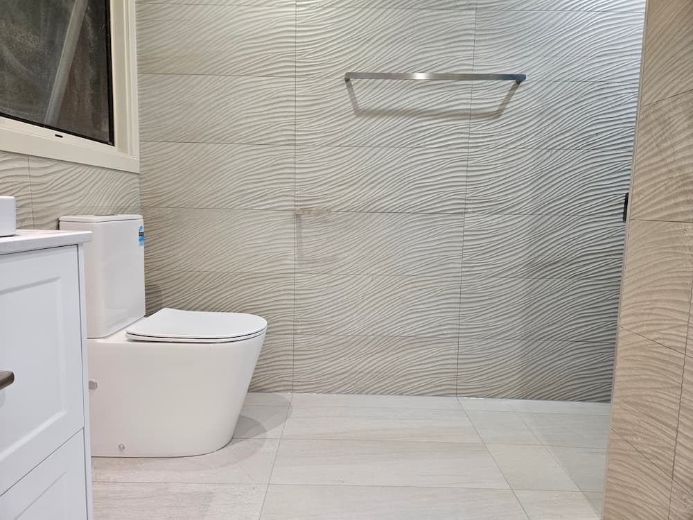 Wall-hung toilet beside textured wave-tile shower wall