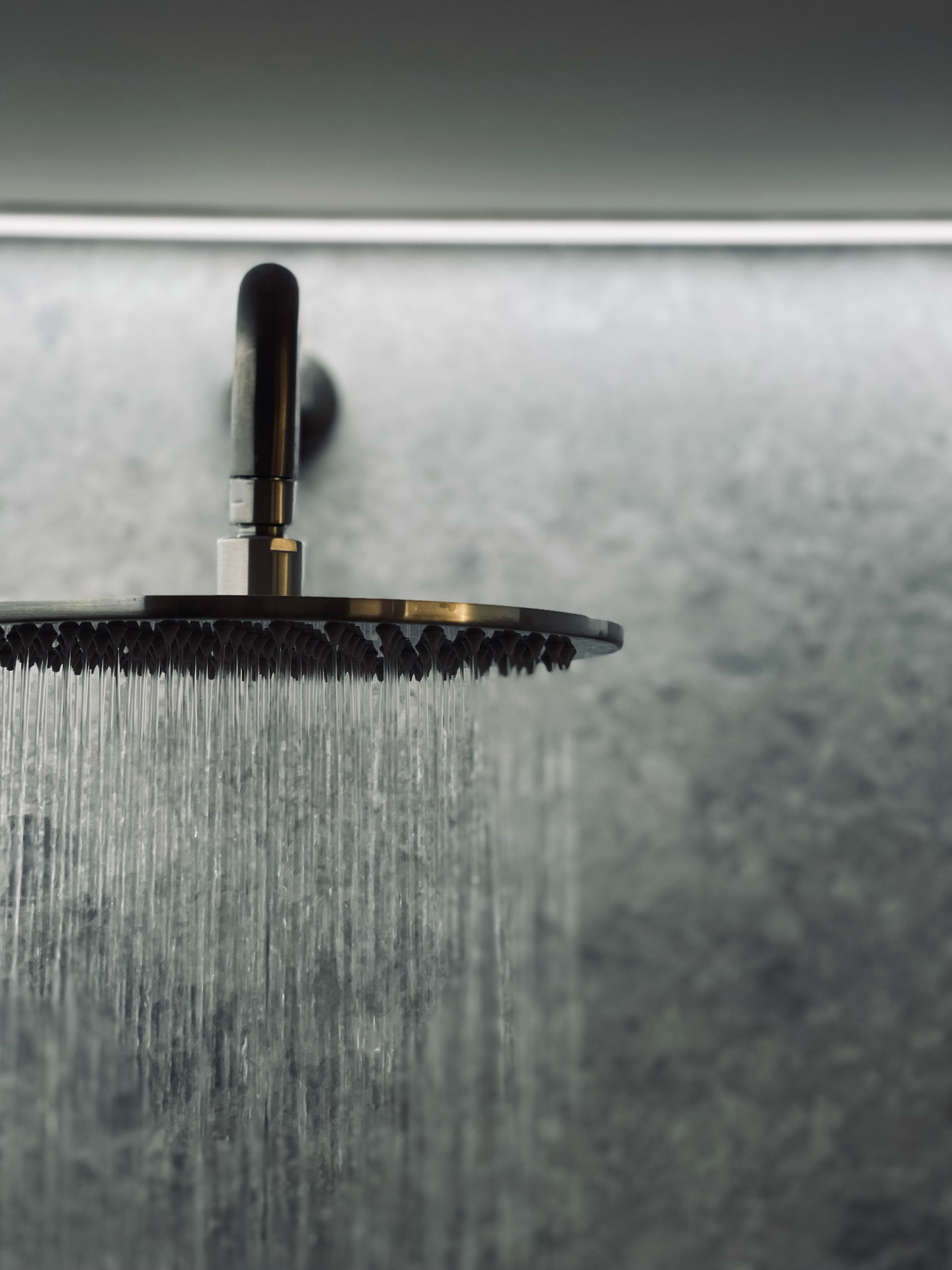 Matte black rain shower head running against a textured stone wall