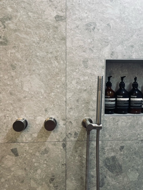 Detail of brushed tapware controls and Aesop niche on terrazzo tiles
